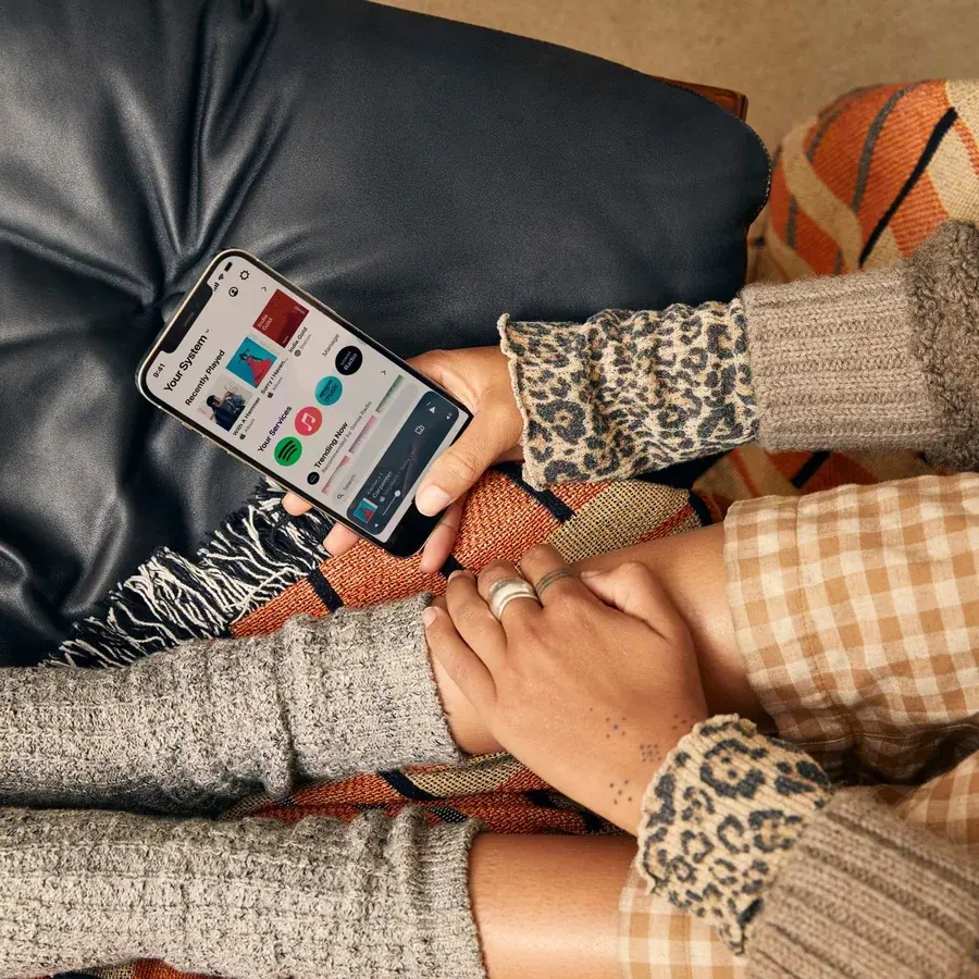 A person using the Sonos app on a phone to control home audio